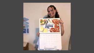 Claire holding up the 2026 calendar with her artwork showing