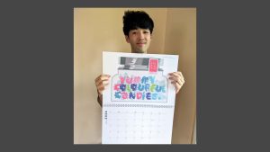 Hikaru holding up the 2026 calendar with his artwork showing