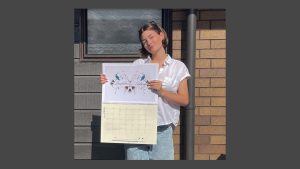 Olivia holding up the 2026 calendar with her artwork showing